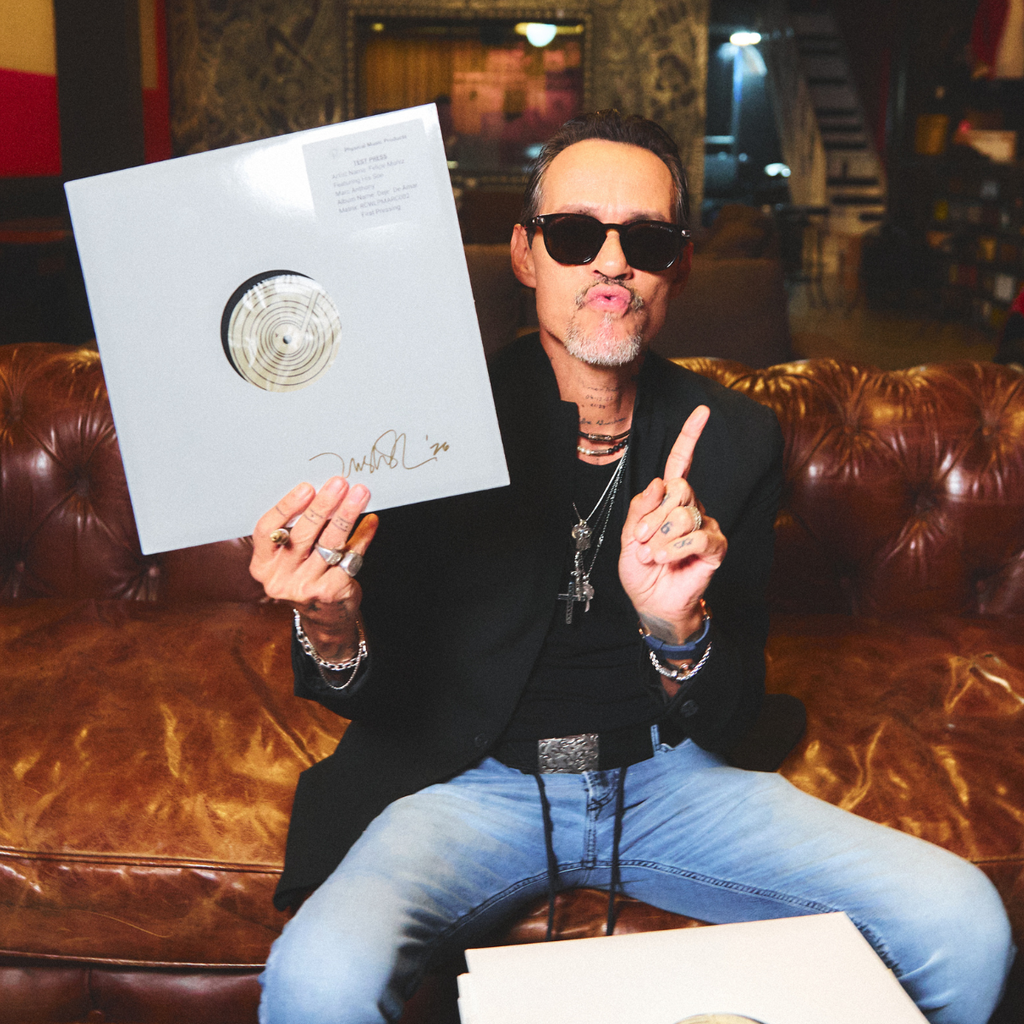 Marc Anthony holding a vinyl record with a gold disc in a room with a couch and decorative wall.