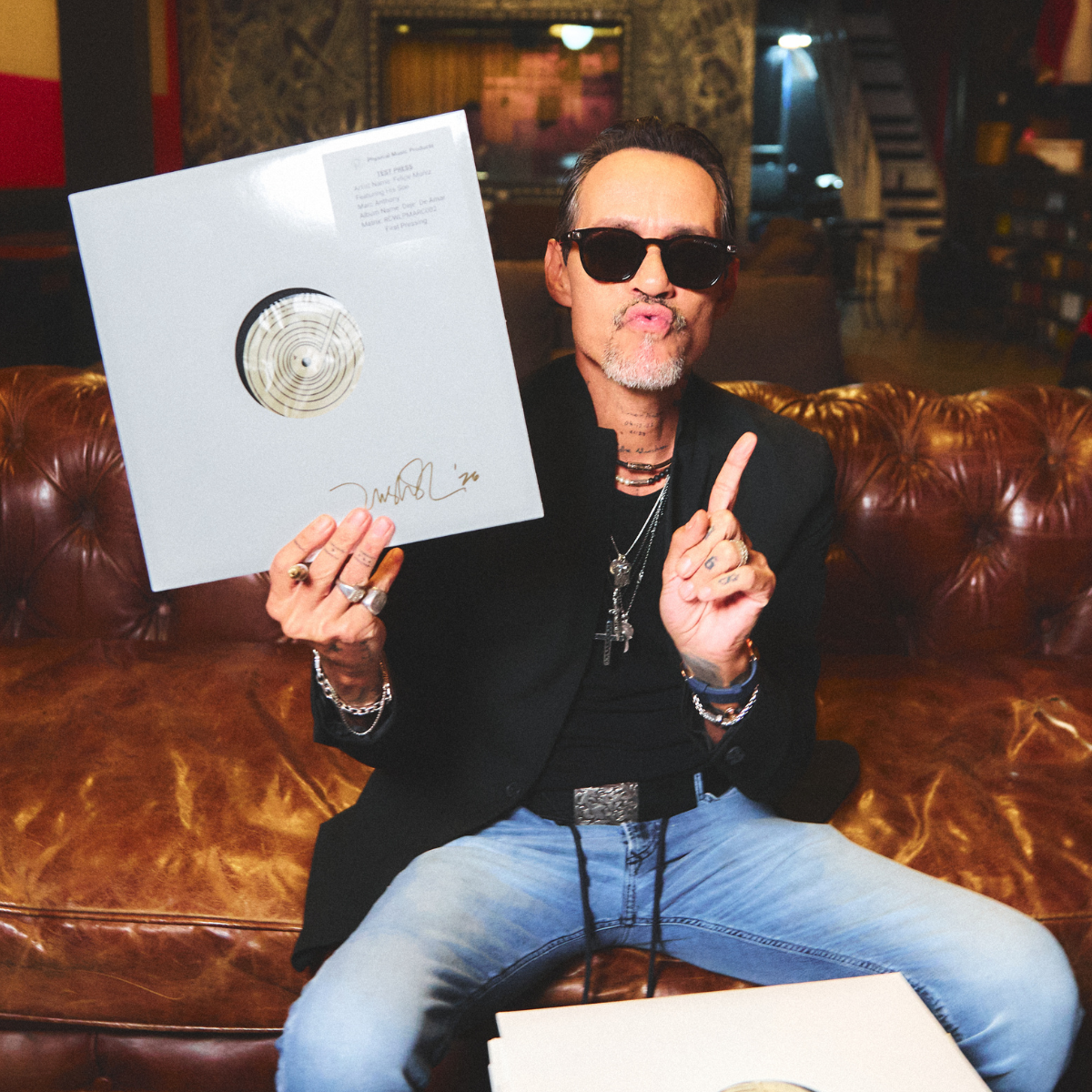 Marc Anthony holding a vinyl record with a gold disc in a room with a couch and decorative wall.